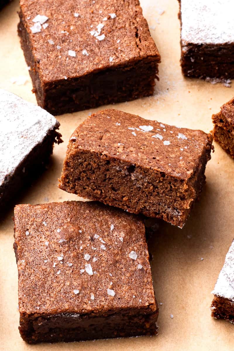 gluten free brownies topped with sea salt stacked on top of each other on brown parchment paper