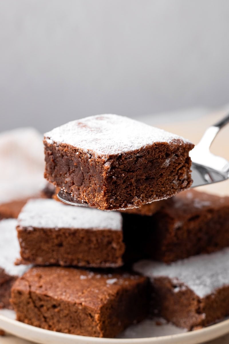 gluten free brownies with powdered sugar stacked on top of each other on a plate