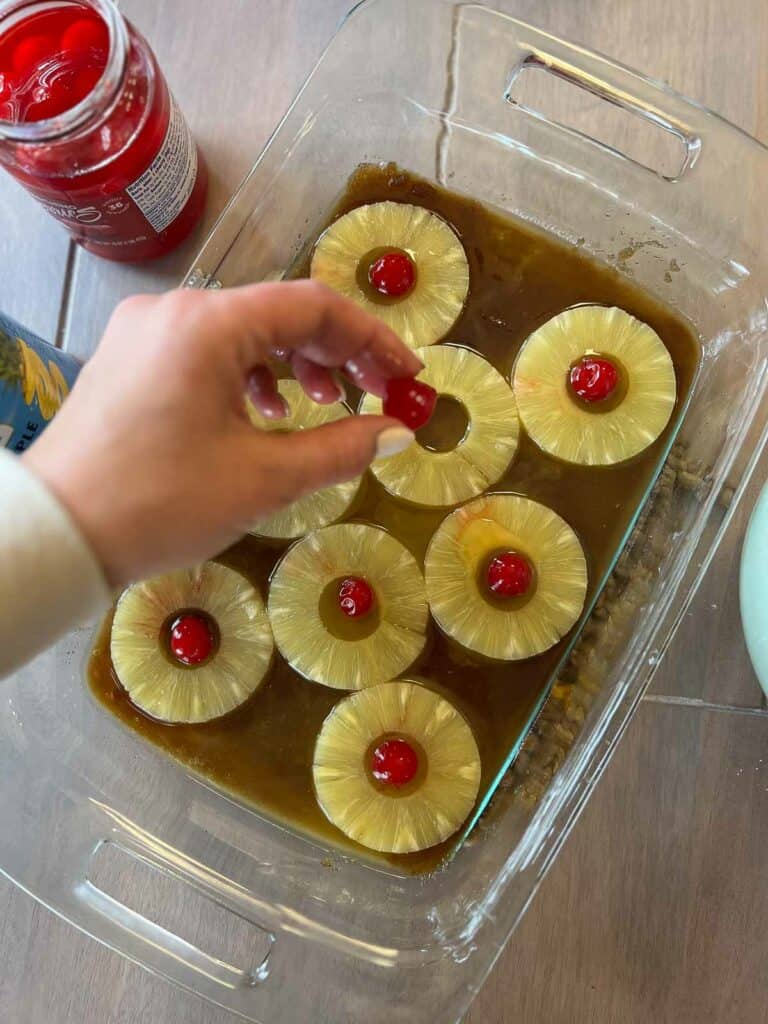 Gluten free pineapple upside down cake being made by pineapple rings and cherries being added to pan
