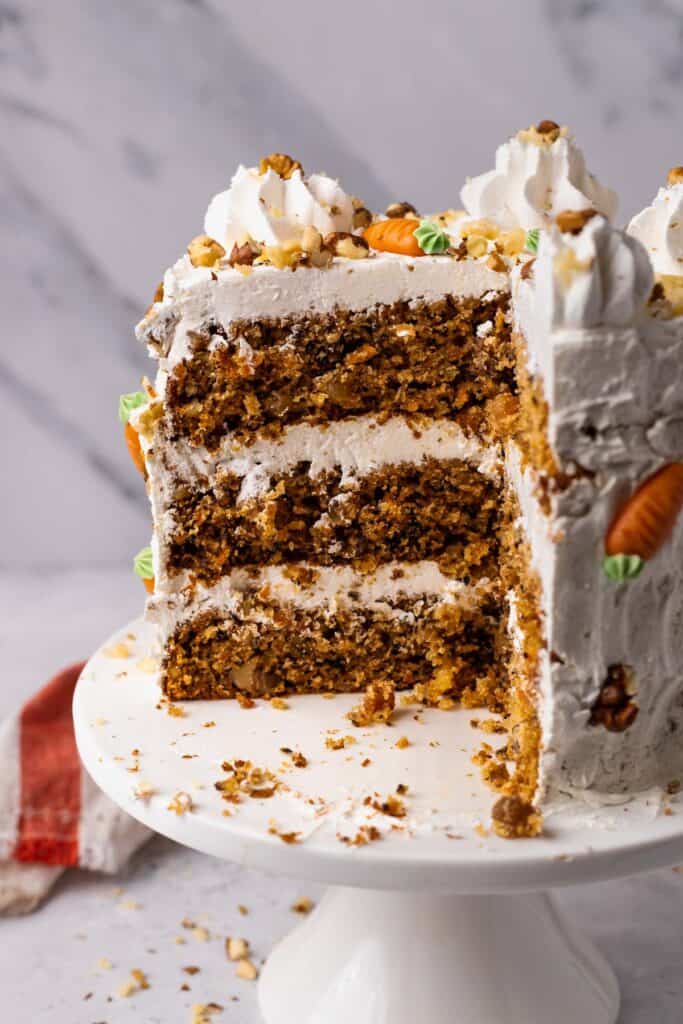 The BEST Gluten Free Carrot Cake on a cake stand with a piece cut out