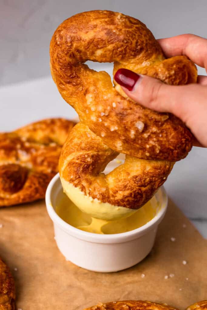 Gluten Free Soft pretzel being dipped into soft, melted cheddar cheese