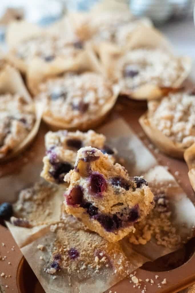 Gluten free blueberry muffins with crumble on top and blueberries near in a pan with one broken in half