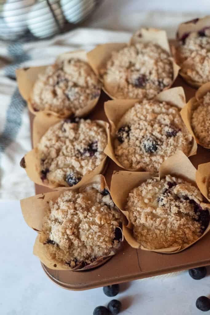 Gluten free blueberry muffins with crumble on top and blueberries near in a pan