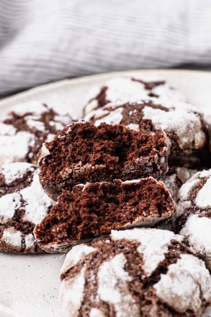 gluten free chocolate crinkle cookies on a plate, one of the cookies is split in half to show the moist texture