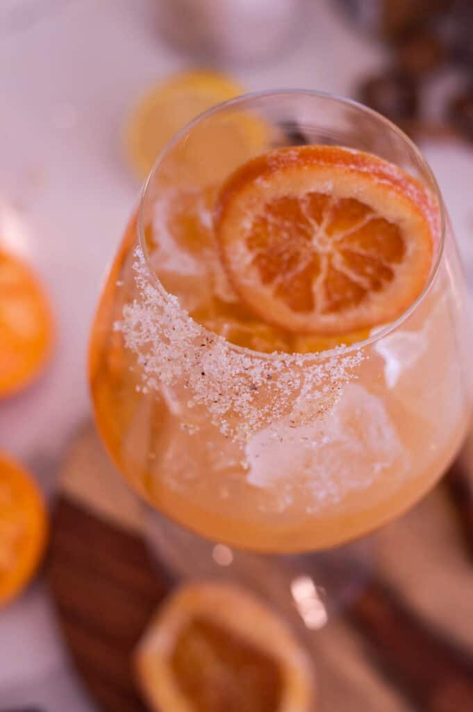 Close up of an orang mocktail in a wide bottom glass with a candied orange slice.