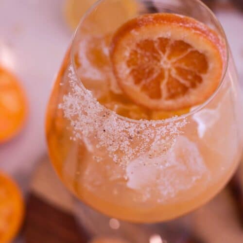 Glass filled with and Orange mocktail with sugar on the front side of the rim and a candied orang slice.
