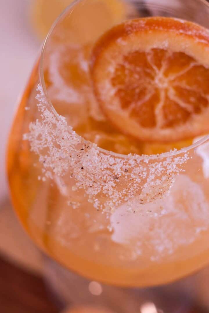 Glass filled with and Orange mocktail with sugar on the front side of the rim and a candied orang slice.