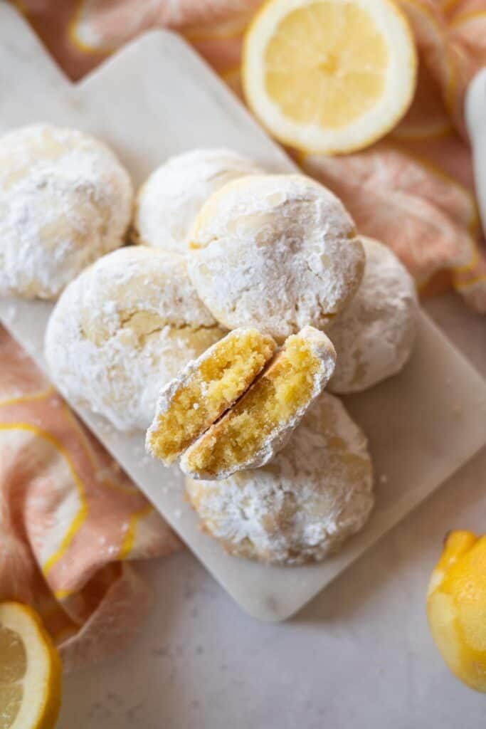 Platter of gluten-free lemon crinkle cookies with the to one broken in half to show the chewy texture in side.