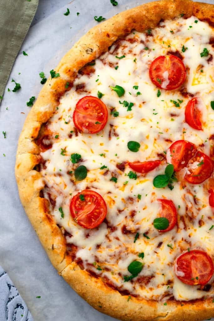 Whole gluten free pizza topped with cheese, tomatoes, and basil.
