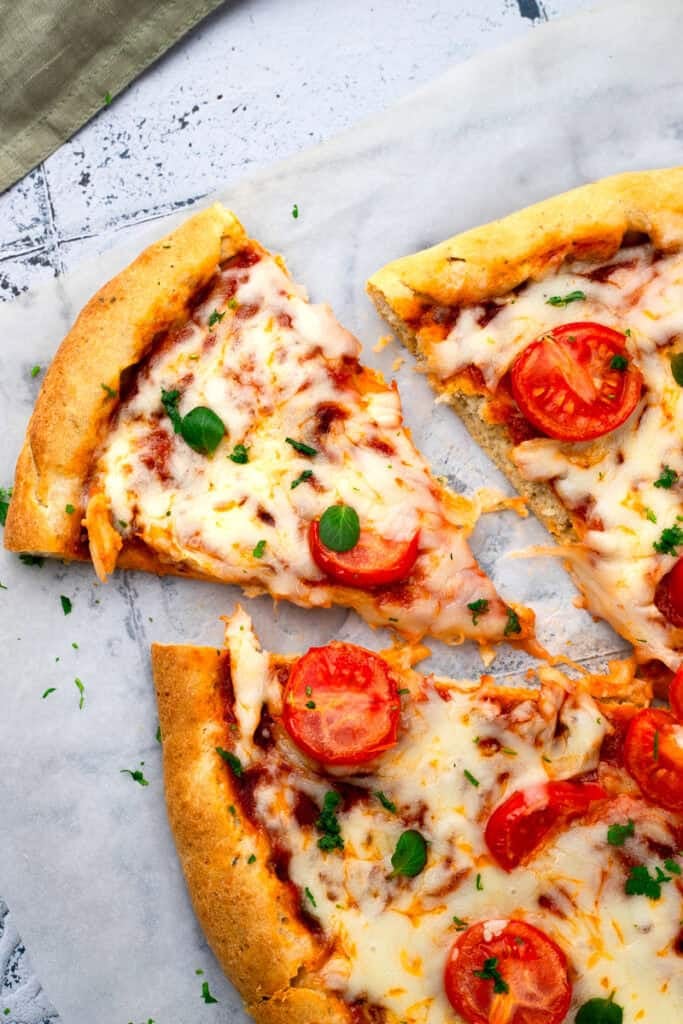 Gluten free pizza on a grey countertop with a slice cut out to show the cheese metled.