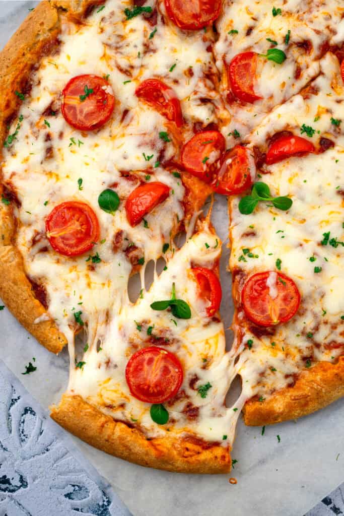 Gluten free pizza on a grey countertop with a slice cut out to show the cheese melted.