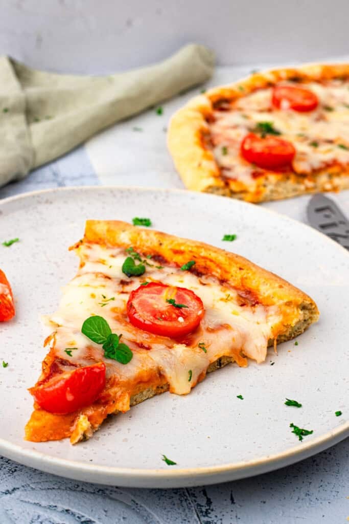 Slice of homemade gluten free pizza topped with cheese, tomatoes, and basil sitting on a plate.