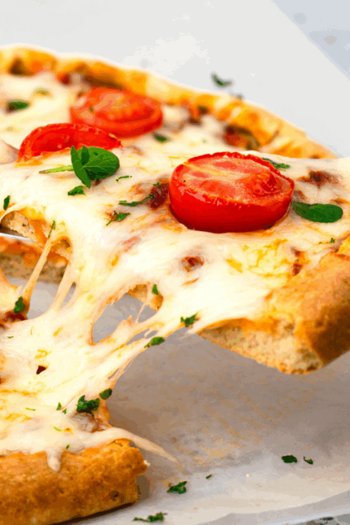 Slice of gluten free pizza on a fork being pulled from a whole gluten free pizza with melted cheese.