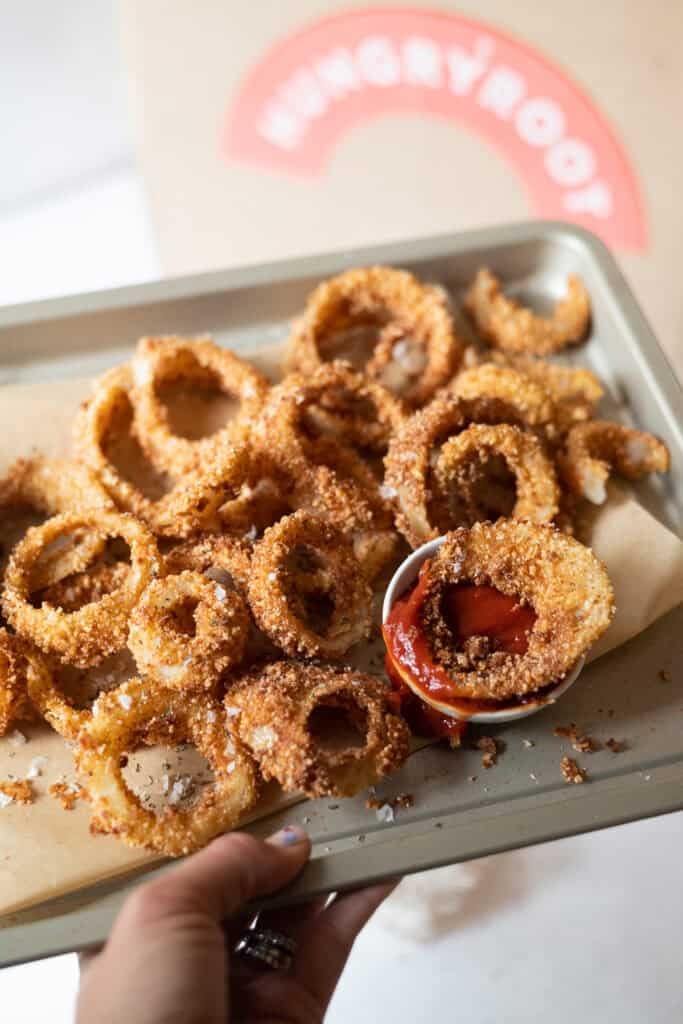 Extra Crispy Gluten Free Onion Rings on a baking sheet with ketchup and salt