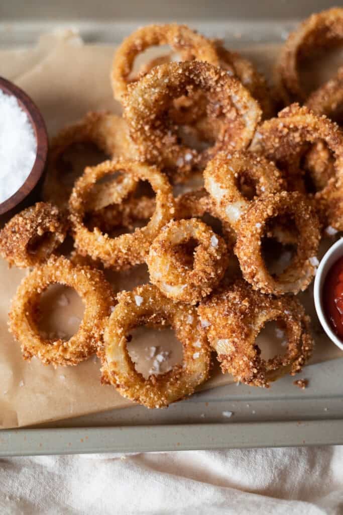 Extra Crispy Gluten Free Onion Rings on a baking sheet with ketchup and salt