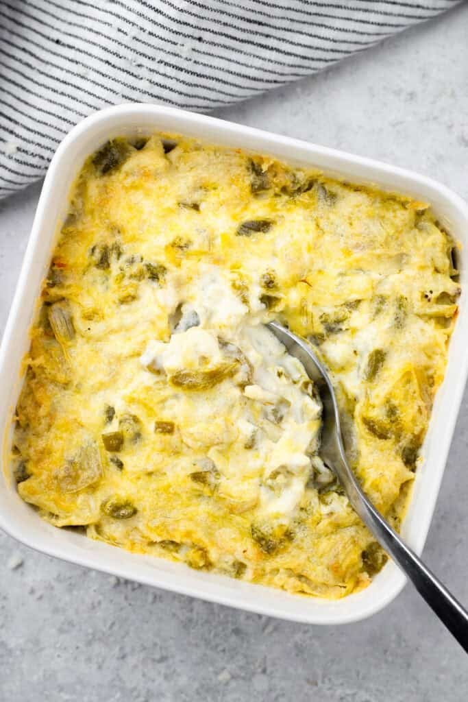 hot artichoke dip baked into a 5x5 square pan and a spoon taking a bite of the artichoke dip out