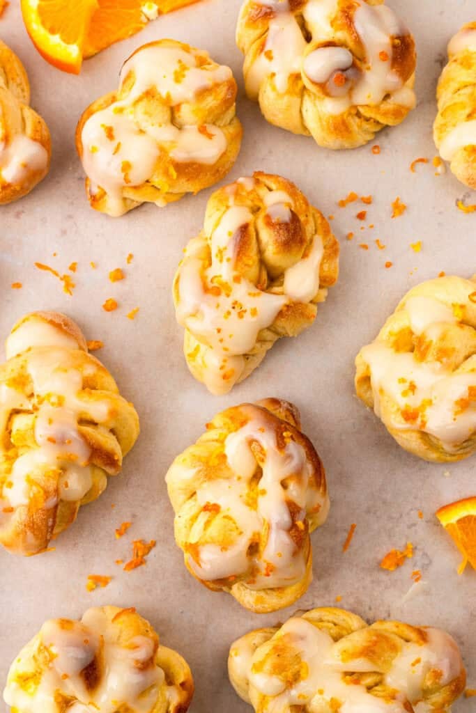 soft and zesty gluten free orange knots on parchment paper with orange zest on top