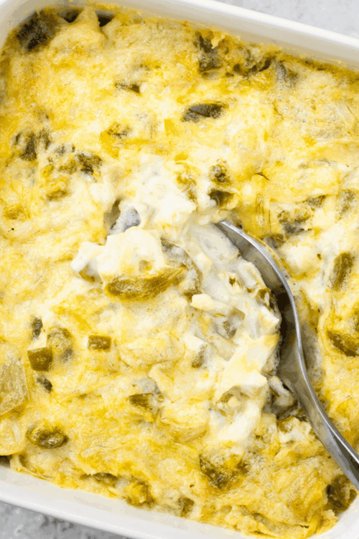 hot artichoke dip baked into a 5x5 square pan and a spoon taking a bite of the artichoke dip out