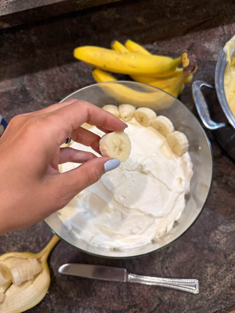Bananas being layered into a trifle dish for gluten free banana pudding 