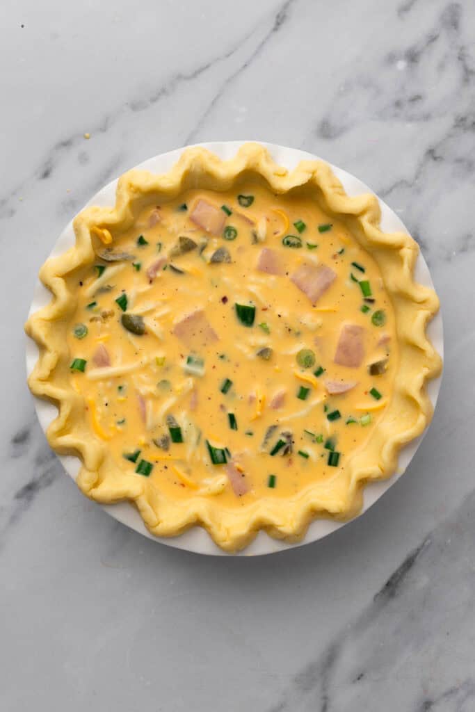 easy gluten free quiche unbaked pie crust filled with ham, egg filling, green chillies and cheese