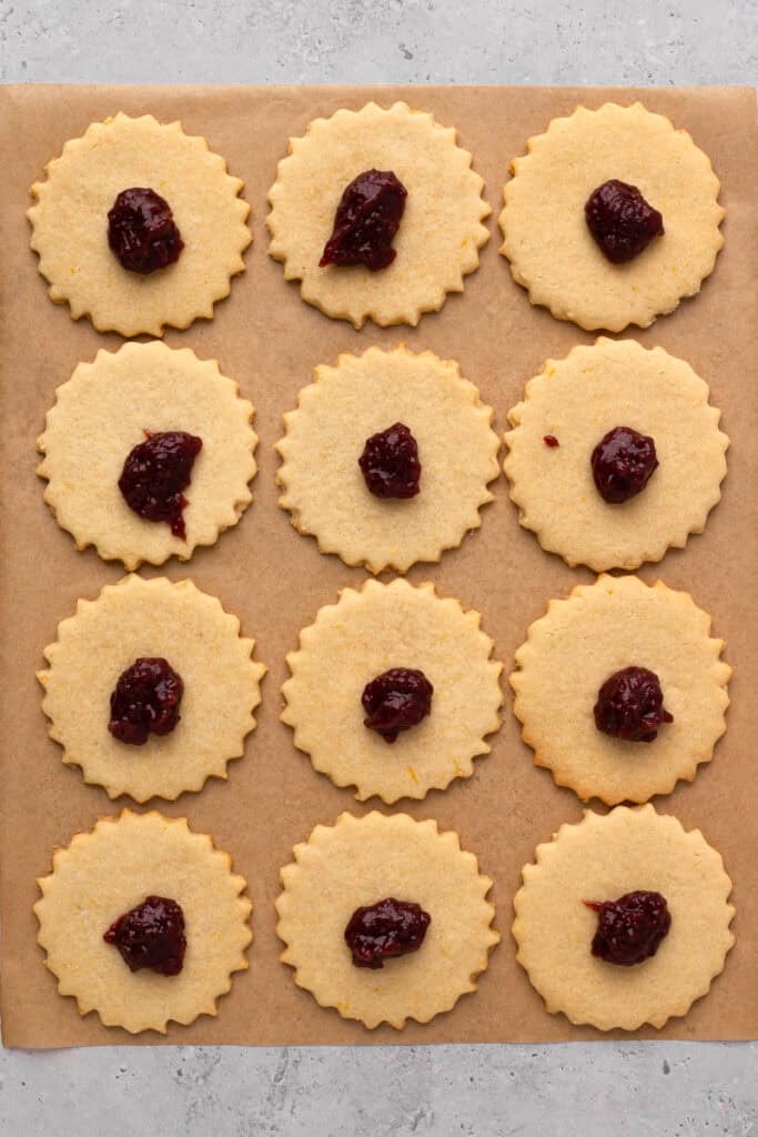 Easy Gluten Free Linzer Cookies on parchment paper before top cookie has been added but with jam