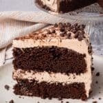 The BEST Gluten Free Chocolate Cake slice cut out, frosted and on a plate with the whole cake in the background.